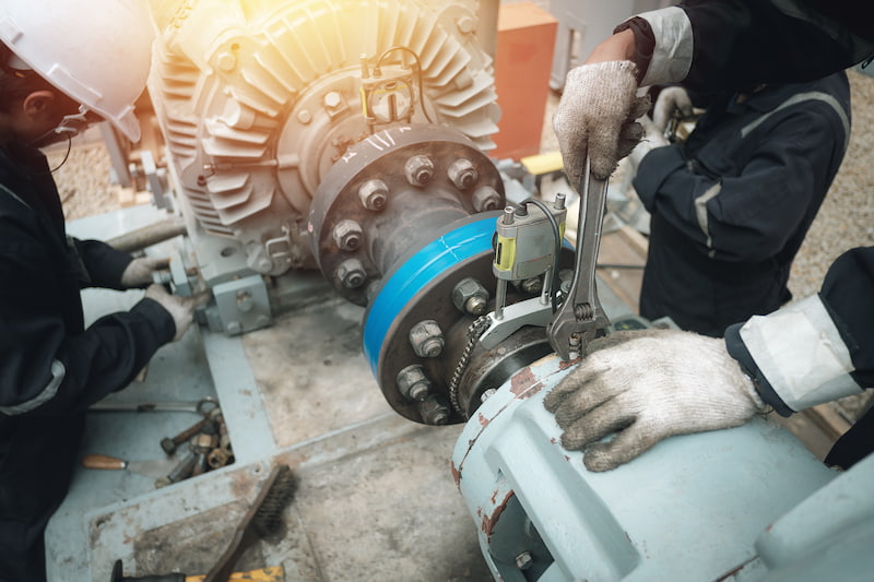 Technicians servicing an industrial pump coupling with spanners