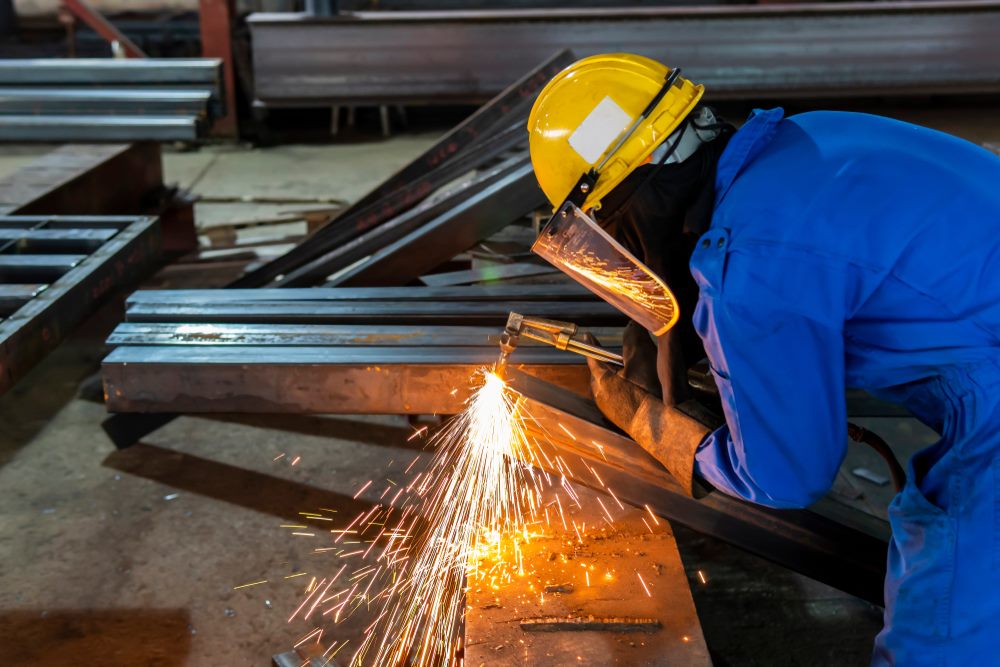 Welder cutting structural steel sections in a fabrication workshop